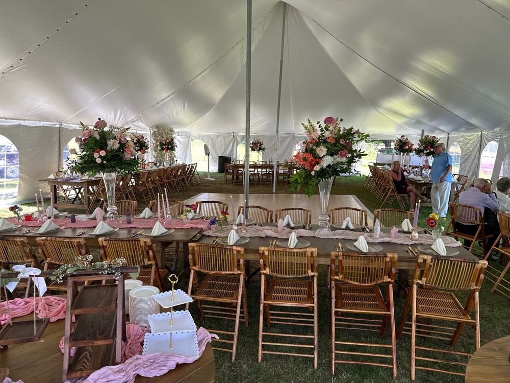 Inside the reception tent: farm tables and bamboo chairs set for a wedding dinner